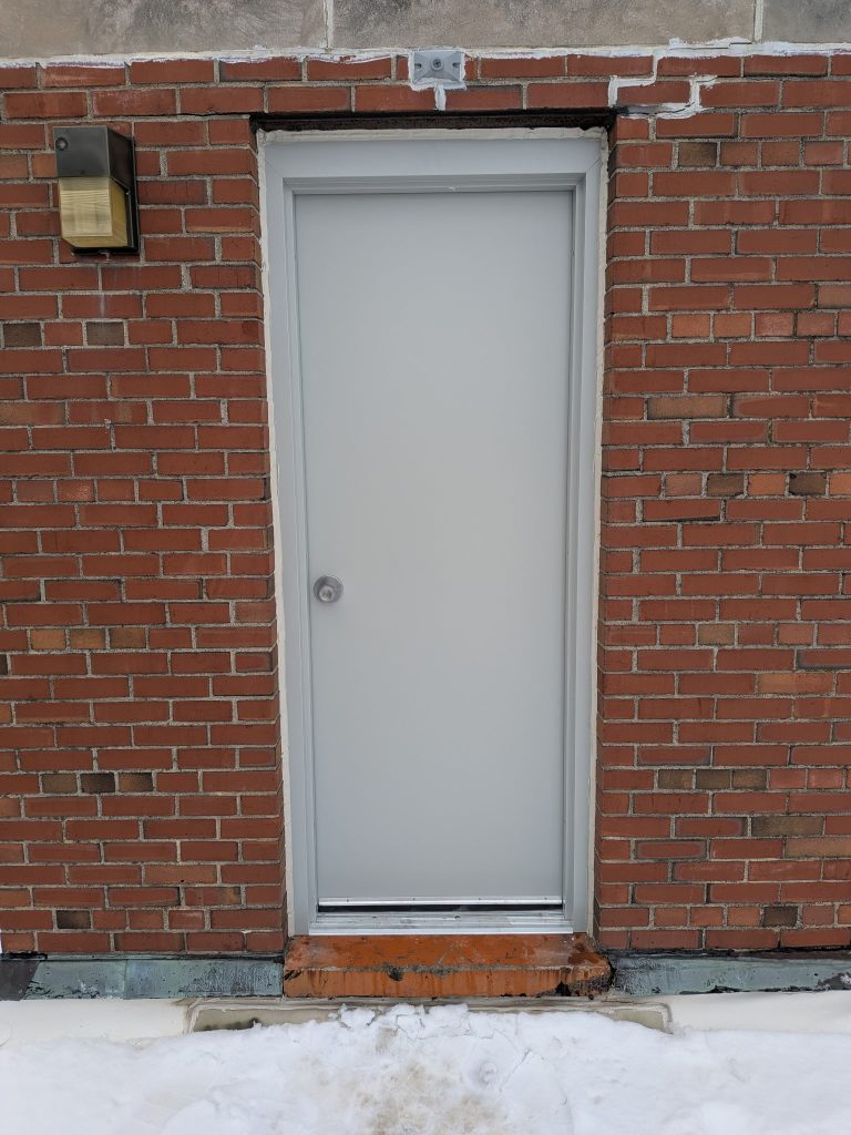 Gray flush steel commercial door installed in a brick wall